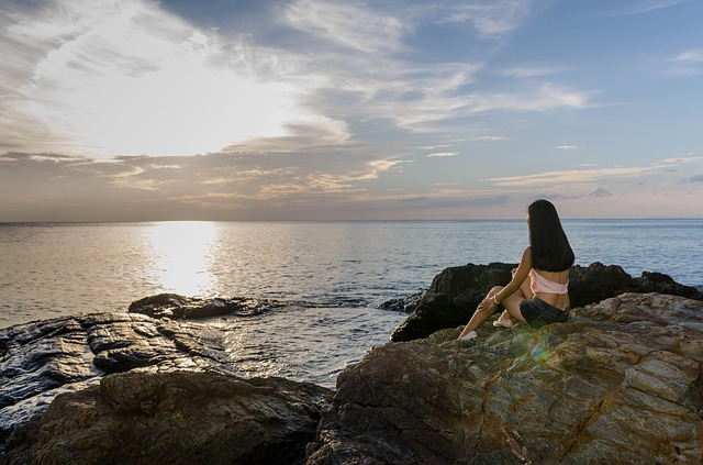 海岸の岩場に座り水平線を見つめる女性