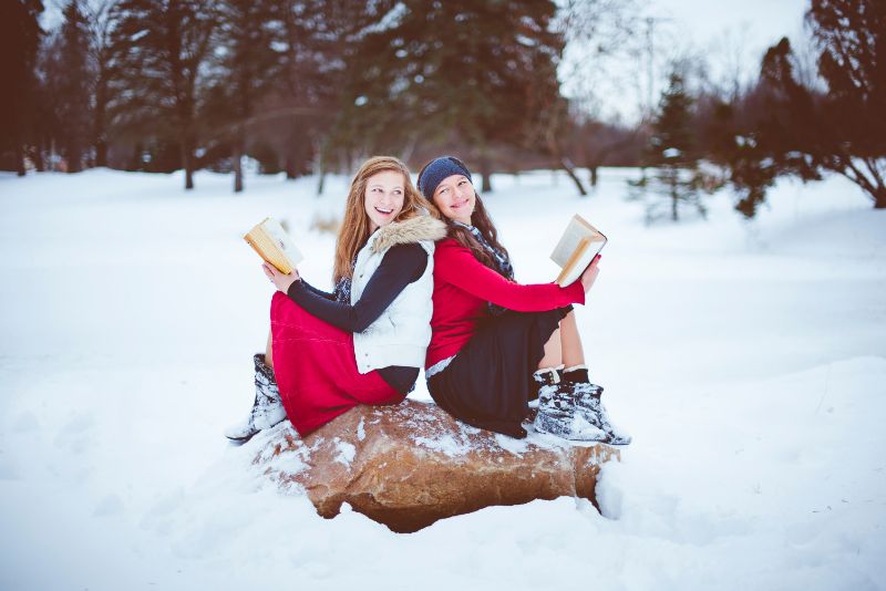 雪国で二人の女性が岩の上で本を読んでいる画像