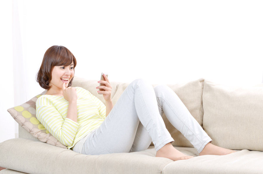 ソファーでスマートフォンを触る女性の画像